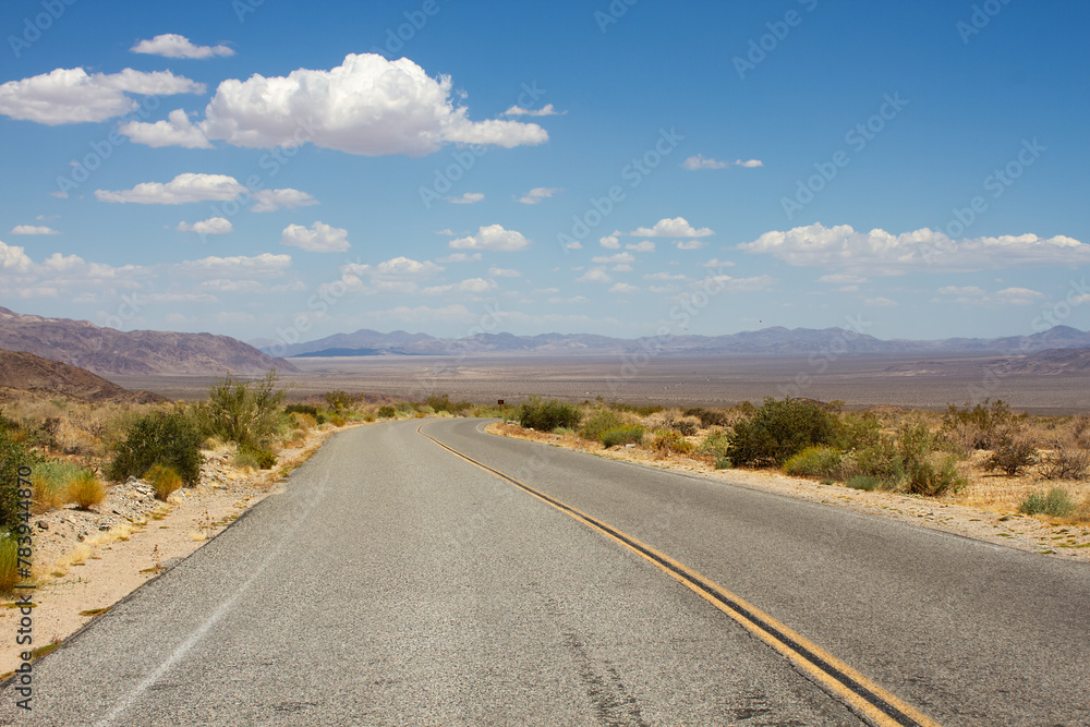 Two lane road through Joshua Tree National Park, California, USA with view of blue sky and mountains