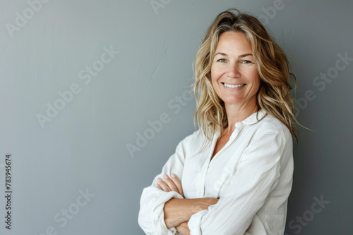 Portrait of a smiling confident woman in her forties, with crossed arms in front of a grey wall background