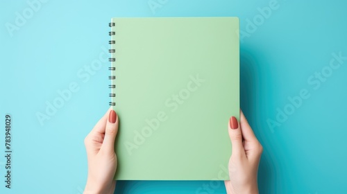 A clean notebook for notes is held by women's hands on a colored background, concepts of education, workplace, creativity. A place for text or advertising.