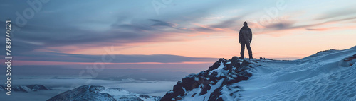 Mans silhouette on snowy mountain peak, dusky sky, cold tones, panoramic view photo