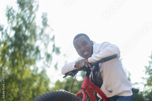 A smiling African-American man with a bicycle in a public park. Sports and recreation