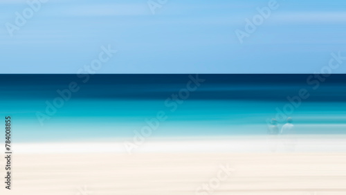 A blurry image of a beach with a man and woman standing on the sand. Scene is calm and serene, with the ocean in the background providing a sense of tranquility