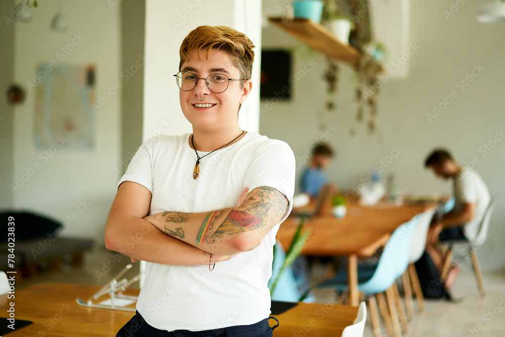 custom made wallpaper toronto digitalTransgender male professional smiles confidently, standing in open office space. Inked arms crossed, happy at work with inclusive team busy in background. Positive workplace for LGBTQ individuals.