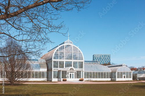 Palm House in Gothenburg city garden, a Victorian style glasshouse, standing elegantly beside a bare tree, concept of historic conservatories and tourism. Gothenburg, Sweden © Photobes