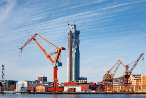 Vivid orange cranes stand tall at Gothenburg port against a backdrop of skyscrapers and blue skies, concept of maritime and industry. Gothenburg, Sweden
