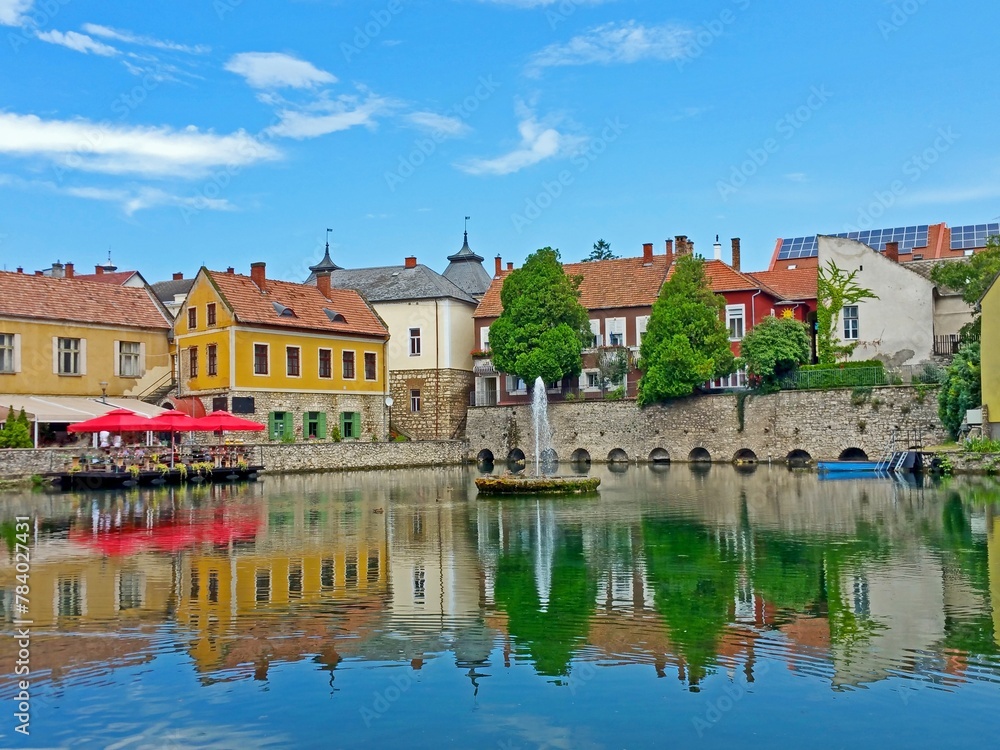 Serene European village nestled in picturesque countryside, with cobblestone paths, blooming flowers, a tranquil river, and a central fountain, creating a peaceful atmosphere for all.