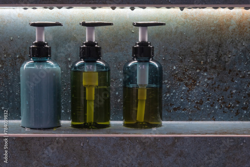 Three bottles of body wash sit in a niche in the bathroom wall. Drops of water are visible on the ceramic tiles. Background. Form.