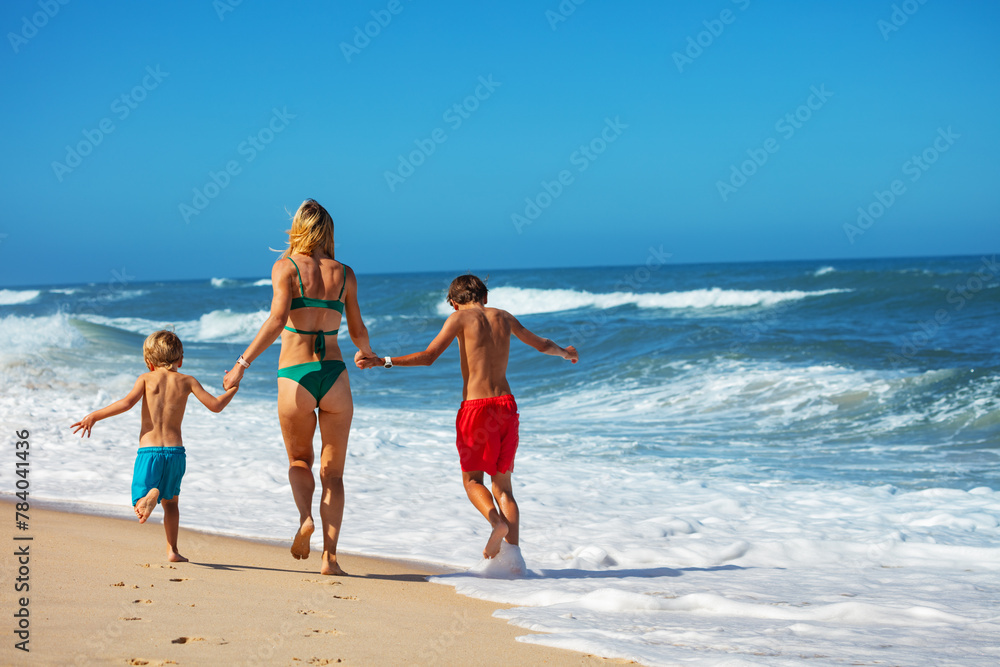 Two boys and a woman in swimwear sprinting joyfully across beach