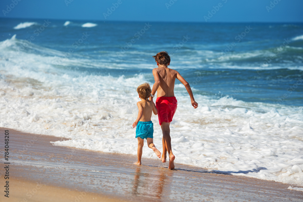 Joyful siblings race by the waterfront on a bright sandy beach