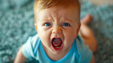 A baby lies on the floor, gazing upward with an intense, angry expression, mouth open wide in a loud scream. The photograph portrays the nature of infancy emotions can be expressed with fervor