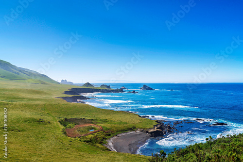 View of coast, ocean, rolling green grass hills, nuclear power plant
