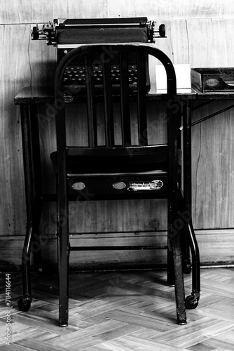 Cadeira de ferro em mesa de madeira e máquina de escrever.  photo
