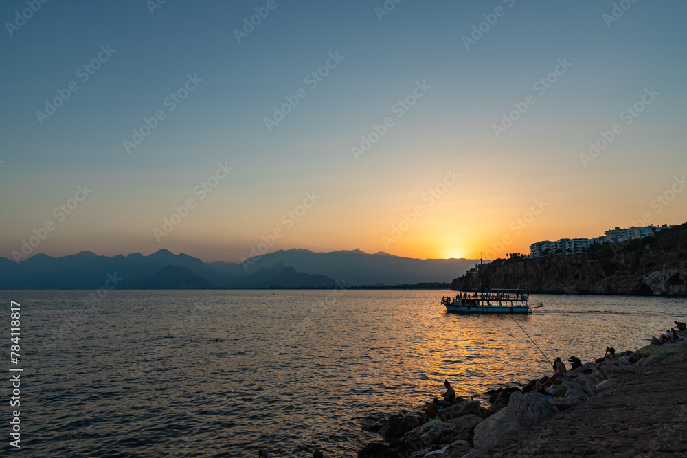 Fototapeta premium ANTALYA, TURKYE - SEPTEMBER 17, 2022: Old harbour in Antalya at sunset with tourists boat at front