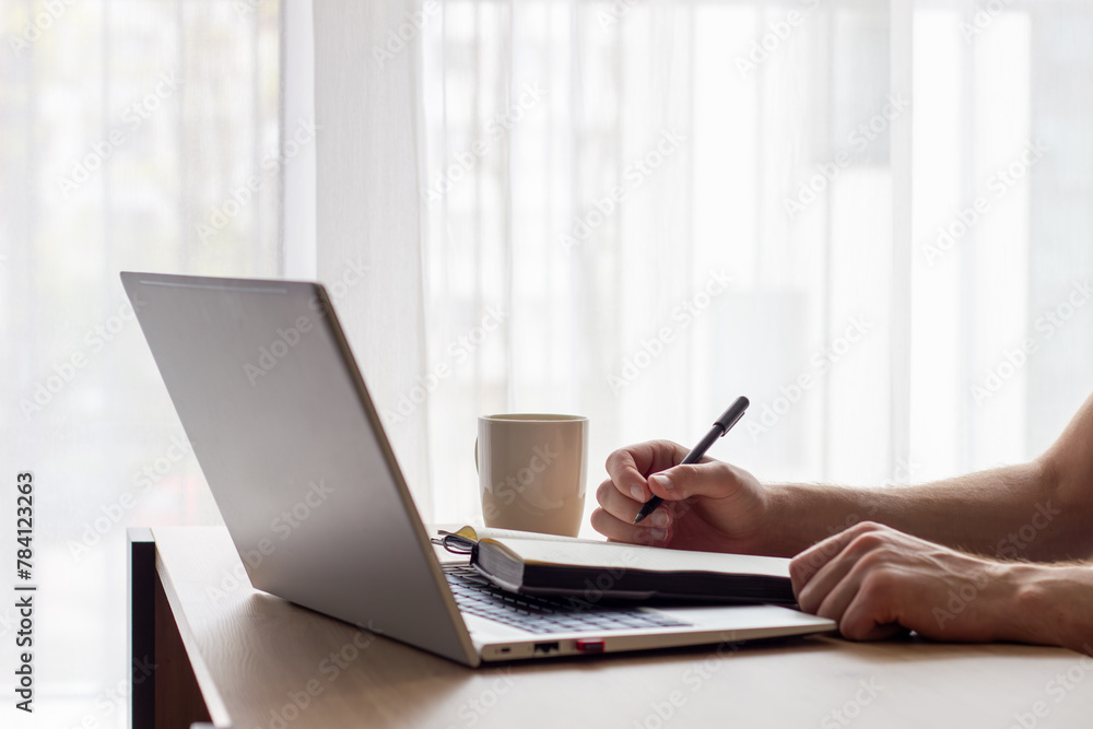 man makes notes in notebook, works with laptop, office routine concept man makes notes in notebook, works with laptop, office routine concept