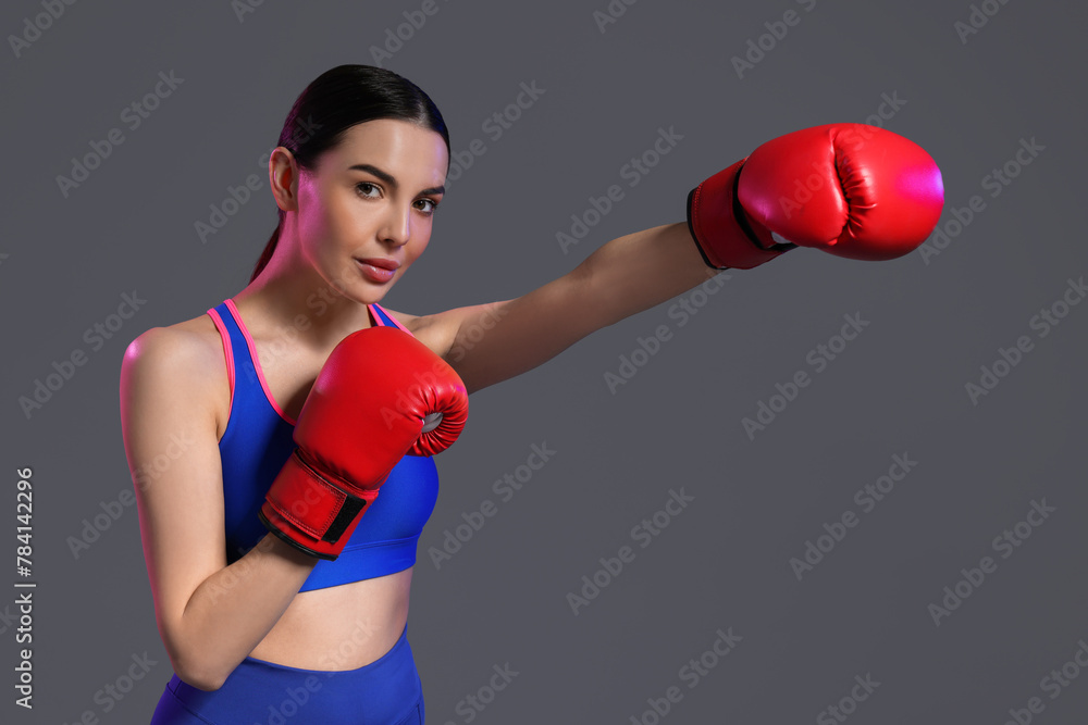 Beautiful woman wearing boxing gloves training in color lights on grey background Beautiful woman wearing boxing gloves training in color lights on grey background