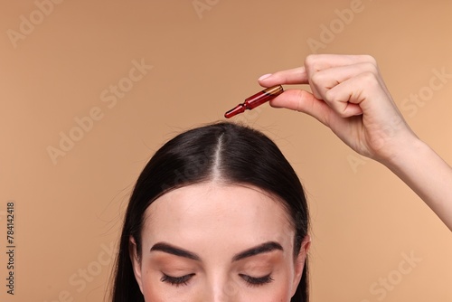 Beautiful young woman using ampoule for hair treatment on beige background, closeup