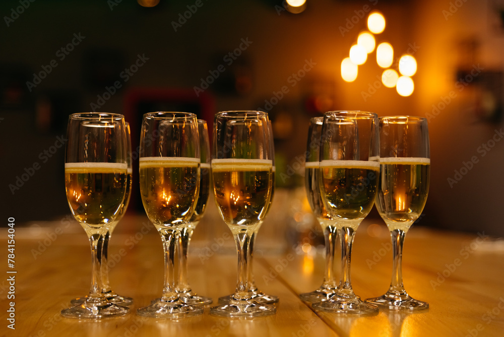 Champagne Glasses on Bar Counter with Warm Ambient Light. Row of champagne glasses filled with sparkling wine, garnished with lime, set on a wooden bar counter against a backdrop of soft glowing light Champagne Glasses on Bar Counter with Warm Ambient Light. Row of champagne glasses filled with sparkling wine, garnished with lime, set on a wooden bar counter against a backdrop of soft glowing light
