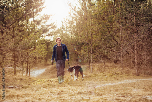 Mature man taking his border collie dog for a walk in the forest