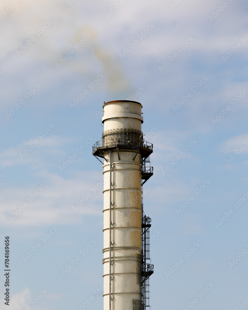 A metal smokestack with a plume of yellow smoke on a cloudy sky A metal smokestack with a plume of yellow smoke on a cloudy sky