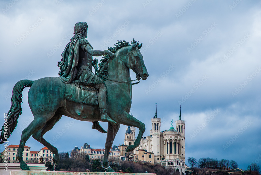 Lyon, France - April 21 2013: Equestrian statue of Louis XIV on Place Bellecour with Basilica Notre Dame de Fourvière in background