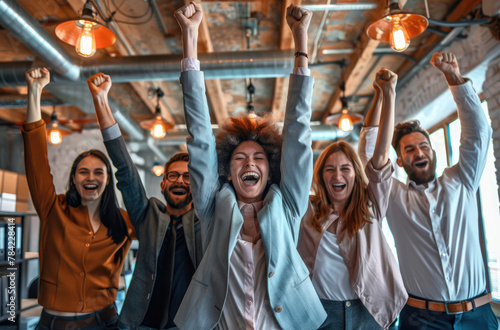 A group of business people are celebrating success in the office, standing with arms raised and smiling at the camera © Kien