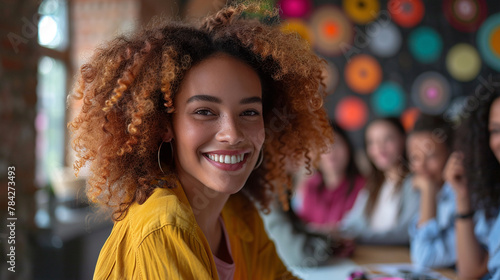 Photo of young smiling woman who is at business meeting in the office. Colleagues are visible on the background