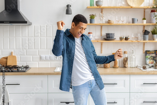 Happy African American man dancing listening to music at home kitchen