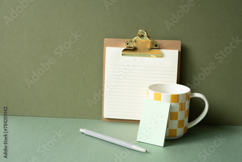 Workspace notepad binder clip, pen, mug cup on green desk. khaki wall background