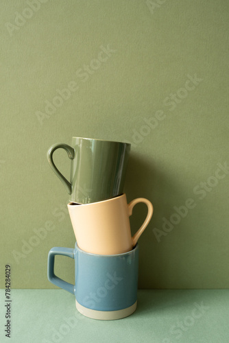 Stack of ceramic mug cups on green table. khaki wall background