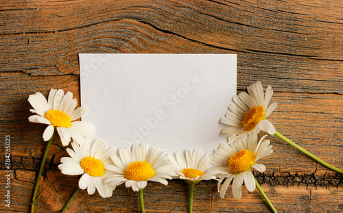 chamomiles on a wooden background with a sheet of white paper, place for text, romantic mood.