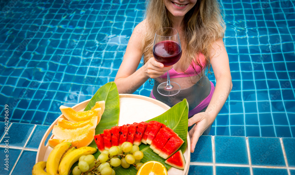 Beautiful woman in the swimming pool with glass of wine and floating tray of fruits Beautiful woman in the swimming pool with glass of wine and floating tray of fruits
