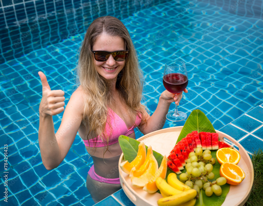 Beautiful woman in the swimming pool with glass of wine and floating tray of fruits Beautiful woman in the swimming pool with glass of wine and floating tray of fruits