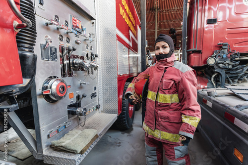 Female Firefighter In Fire Protection Suit standing at fire station photo