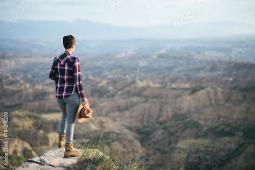 Woman in a plaid shirt and hat looking at the landscape from above. photo