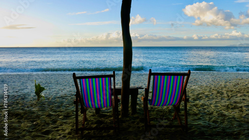 Empty sun loungers on the sandy beach. Two empty sun loungers under a beach umbrella are turned towards the sea. © Houston