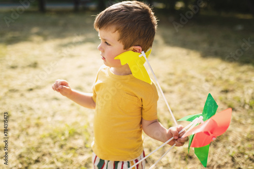 A happy 3-4 year old boy runs on the grass in the summer with a colorful pinwheel. Carefree childhood