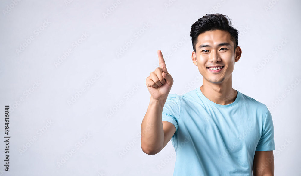 Fototapeta premium a smiling young man in a blue shirt is pointing upwards, asian male, pointing index finger, isolated white background, website banner, copy space, background