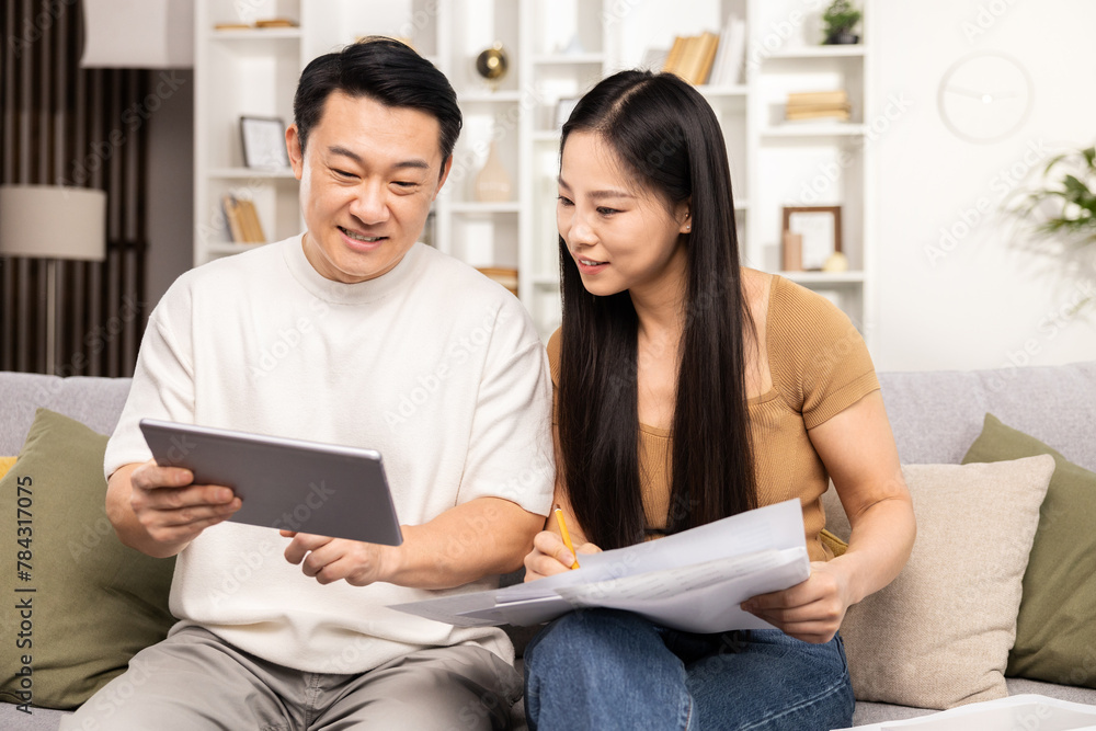 Couple planning budget with digital tablet and documents, sitting on couch at home, peaceful financial decision making Couple planning budget with digital tablet and documents, sitting on couch at home, peaceful financial decision making
