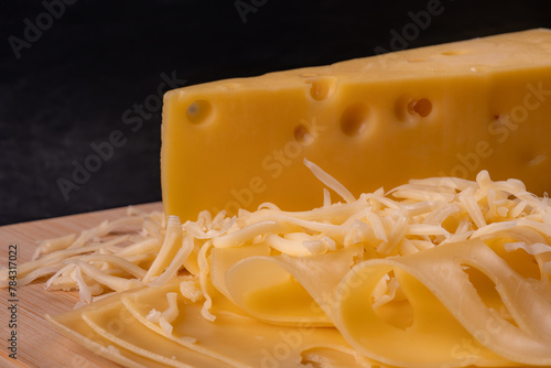 A piece of cheese, cheese slices and grated cheese lie on a cutting board.