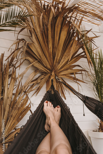 Woman chilling and relaxing in cozy hammock. Summer holiday travel vacation concept. Aesthetic bohemian scene with female legs