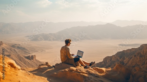 Man with laptop sitting on top of a mountain. © vlntn