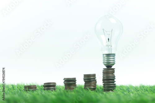 A stack of pennies on a green field with a light bulb on top