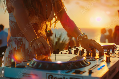 Beautiful female DJ playing music at sunset on the beach with people dancing in the background
