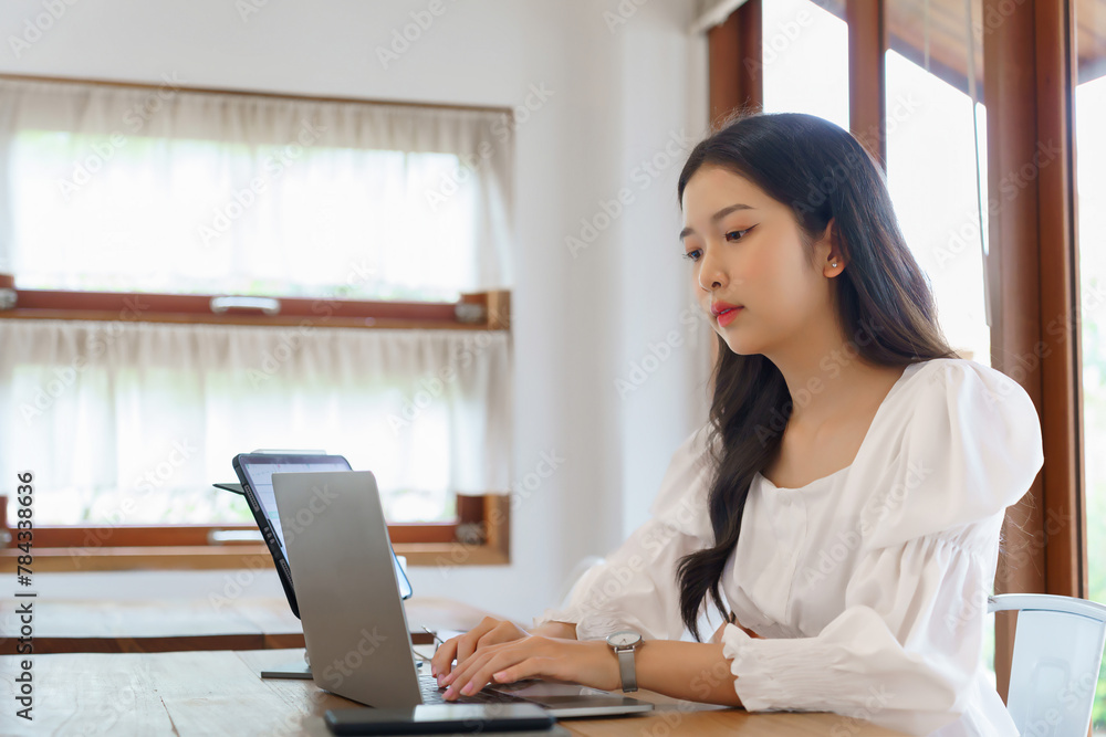 Young asian businesswoman typing business report on laptop and reading financial data on tablet while analysis strategy about investment and planning of new startup project to working in cafe Young asian businesswoman typing business report on laptop and reading financial data on tablet while analysis strategy about investment and planning of new startup project to working in cafe