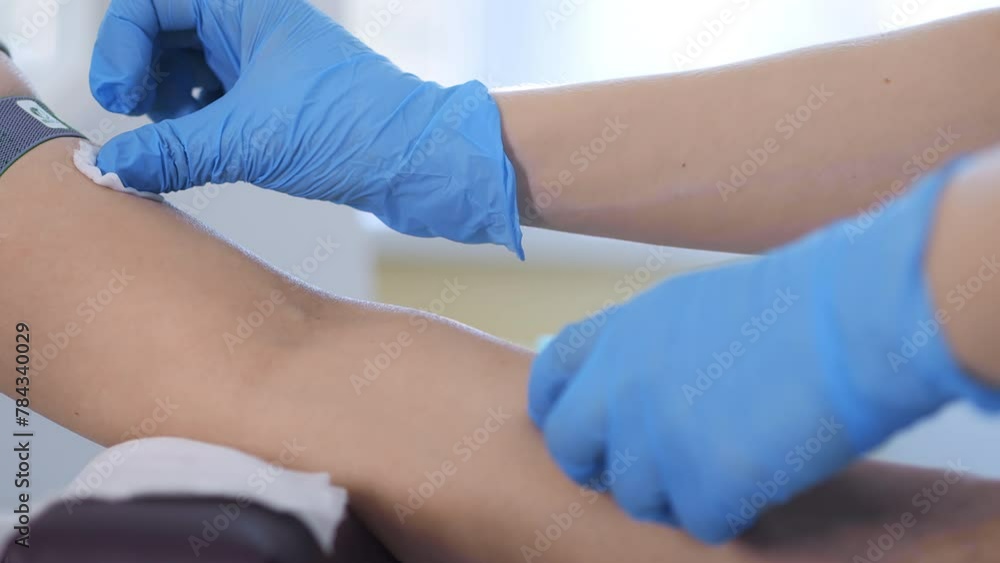 A doctor in a blue medical glove holders cotton wool with medical alcohol and wipes the place where he will take blood for analysis. Female doctor prepares arm for makes injection. A doctor in a blue medical glove holders cotton wool with medical alcohol and wipes the place where he will take blood for analysis. Female doctor prepares arm for makes injection.