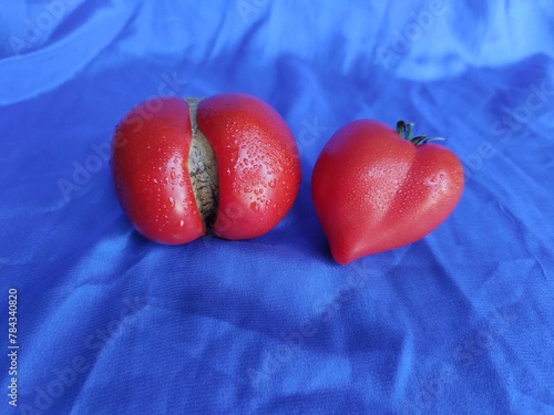 heart-shaped tomato on a white plate. red tomatoes on a blue background