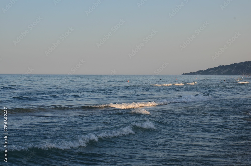 Beautiful scene of the blue sea waves surrounded by hills under the pink sky in the daytime