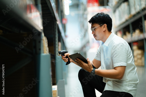 A man is looking at a tablet while standing in a warehouse. He is wearing glasses and he is focused on the tablet