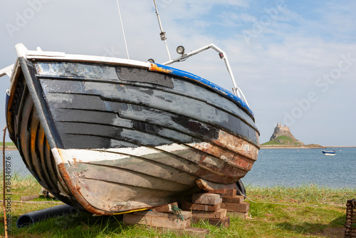 Lindisfarne, Holy Island, Northumberland, UK: traditional old fishing boat in the foreground, and the castle and harbour beyond