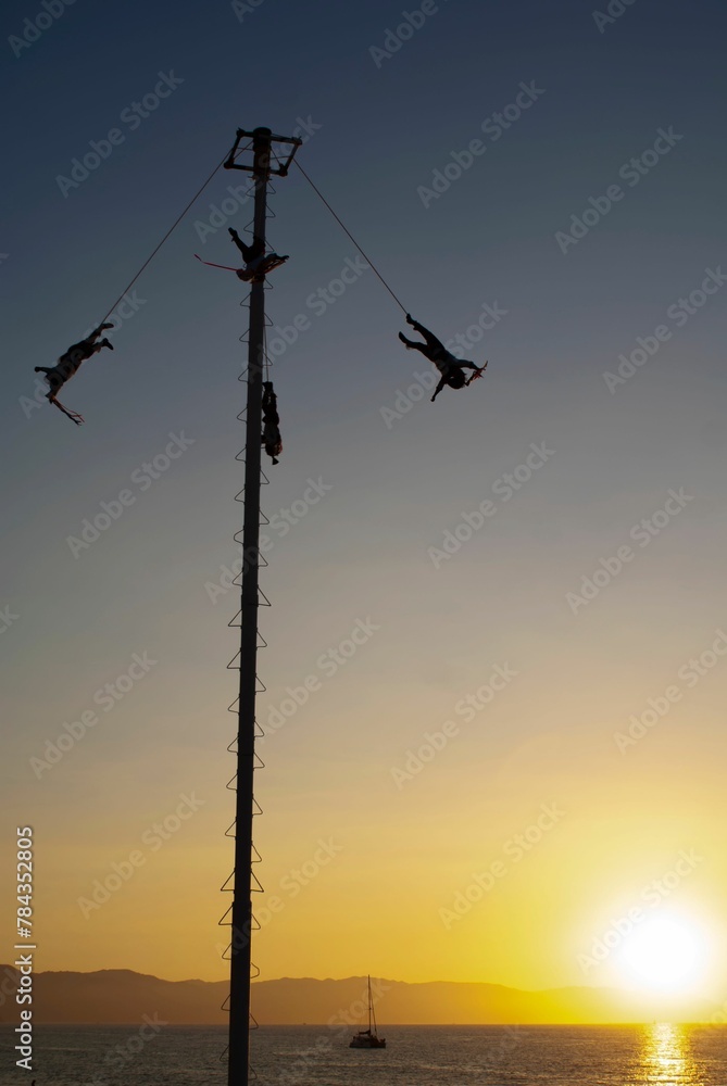 Silhouette of people enjoying Voladores de Papantla (flying men) at sunset with a seascape view Silhouette of people enjoying Voladores de Papantla (flying men) at sunset with a seascape view